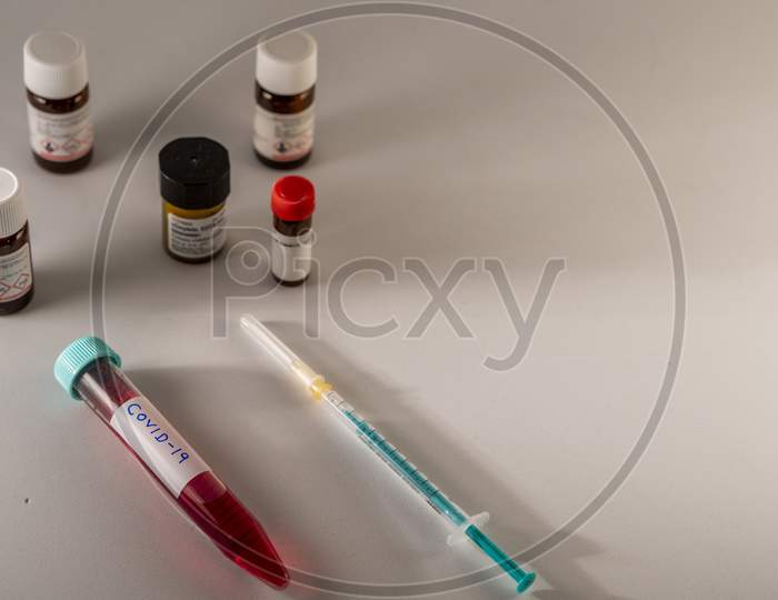Photo concept shows Covid-19 sample in a falcon, and chemicals, and syringe in a blurred background.