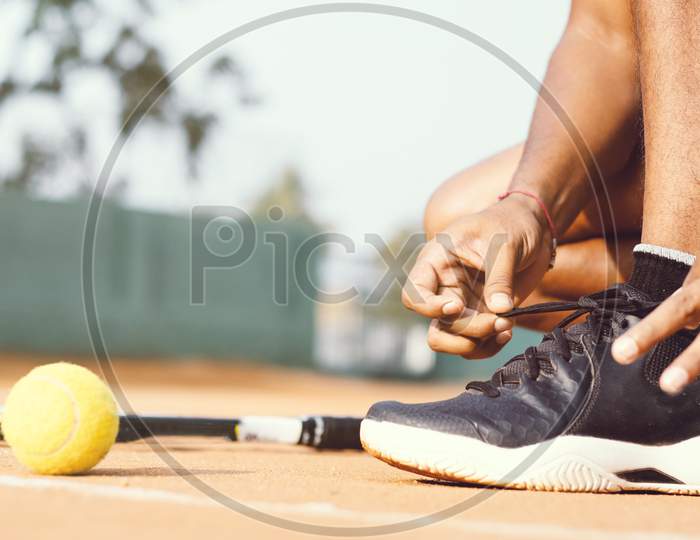 Close up shot of a Young Indian Man tying Shoelace in a Tennis Court