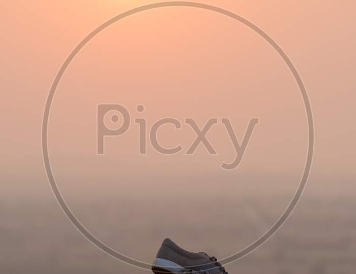 A pair of shoes on the edge of rock With Sun In Background