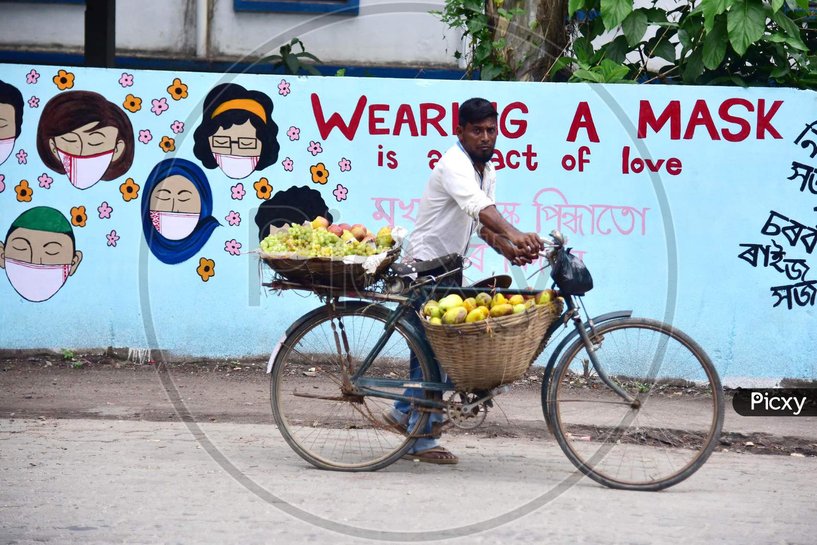 A Fruit Vendor Pushes His Bicycle  In Front Of a Wall Graffiti Of COVID-19  In Nagaon District Of Assam On June 8,2020