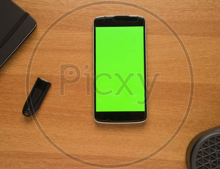 Smartphone With Green Screen Mock Up On Table With Bluetooth Speaker, Pendrive And Diary Book