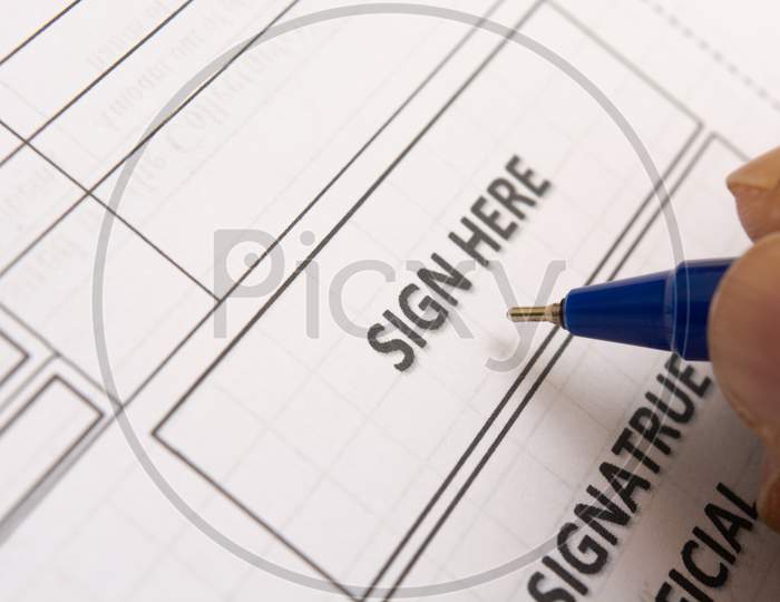 Close Up Of Fingers Holding A Pen And Signing A Income Tax Form.