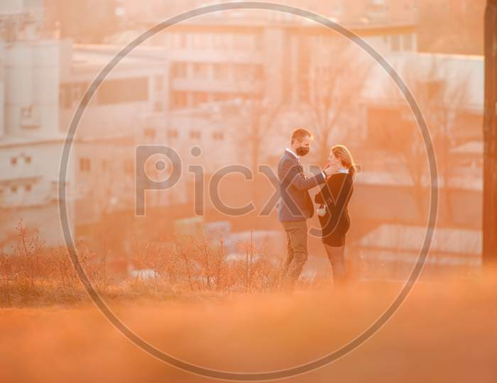 Couple in love on a suburban meadow at sunset. A man in a cloth face mask took off the mask of his pregnant wife for a kiss.