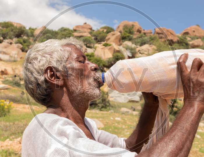 Close Up Of Thirsty Farmer Man Drinking Water From Plastic Bottle Covered With Cloth For Cooling During Hot Sunny Day.