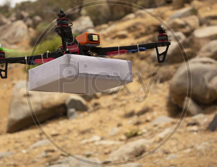 Assembled Drone Quadcopter Delivering A Package With Moutain As A Background