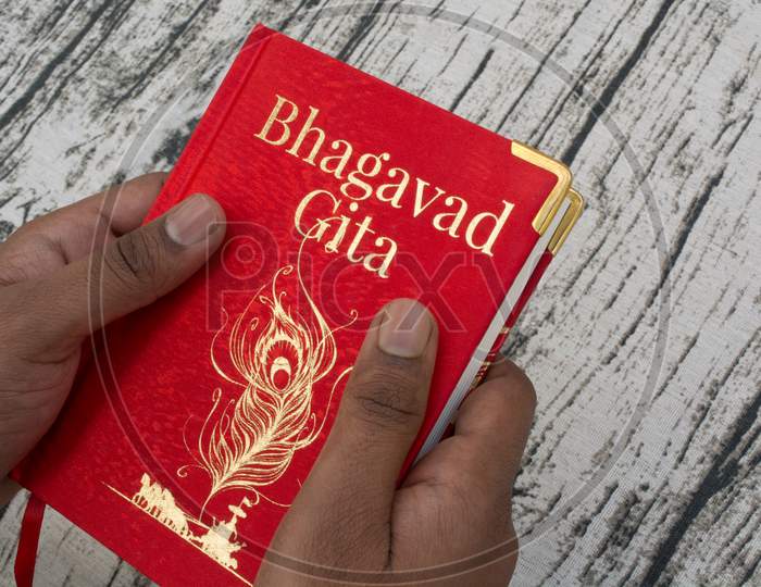 Holding Bhagavad Gita With Hands On Textured Background
