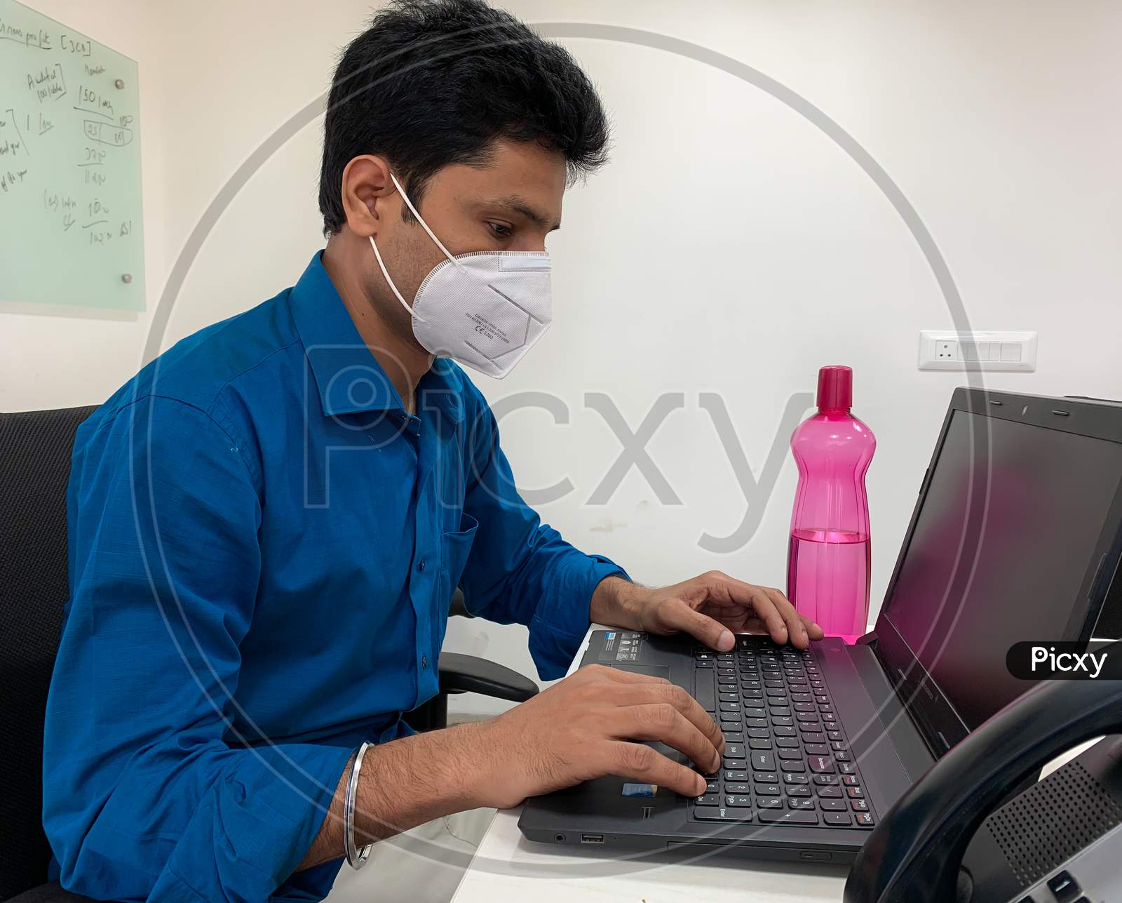 Man With Mask On Face Working On Laptop At Office.