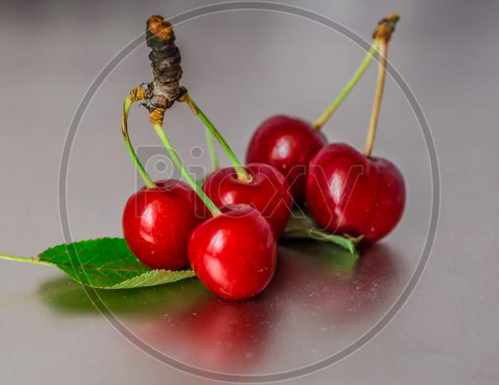 A shot of fresh cherries with green leaves on the smooth surface