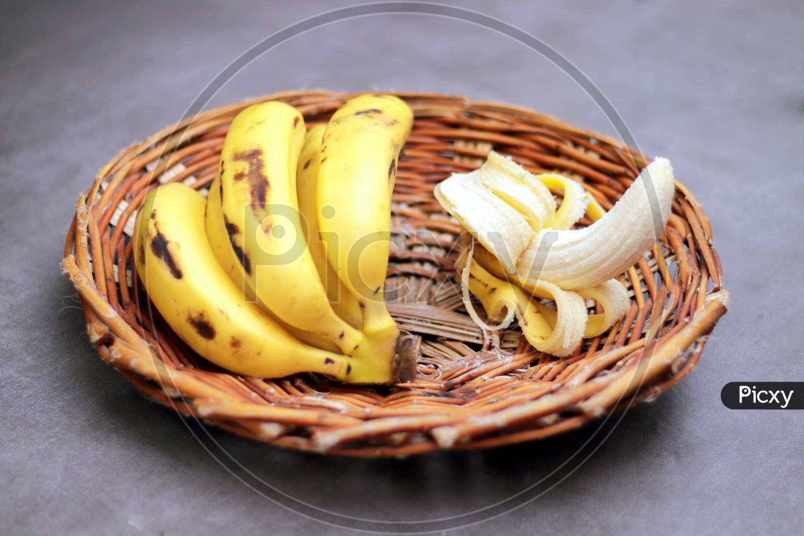 Bunch of bananas in a wooden basket, one unpeeled banana.