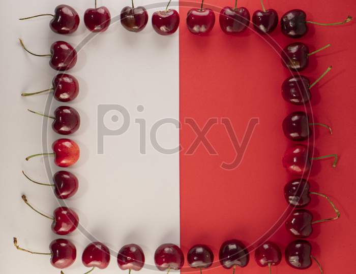 Frame made up of fresh red cherries on a red and white background. Photo has empty space for text