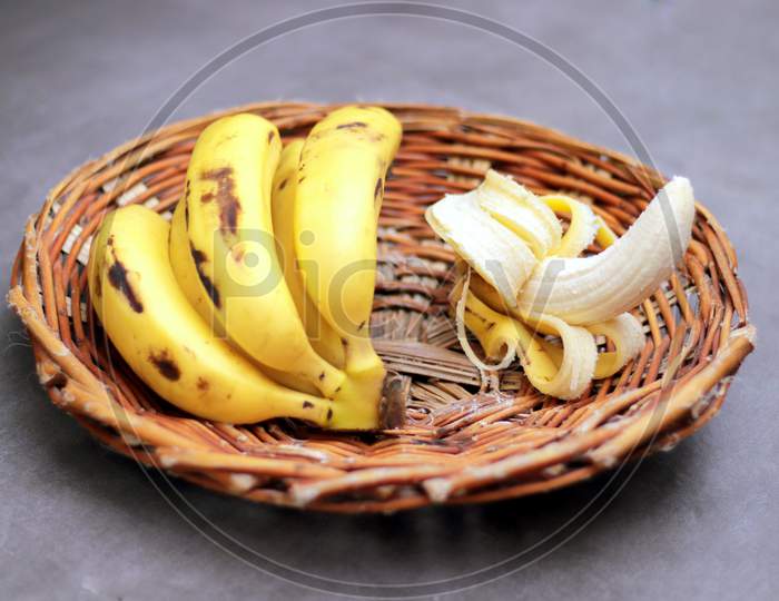 Bunch of bananas in a wooden basket, one unpeeled banana.