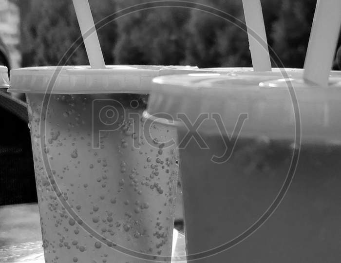 Monochrome picture of two glass of soda with straw and trees on the background.
