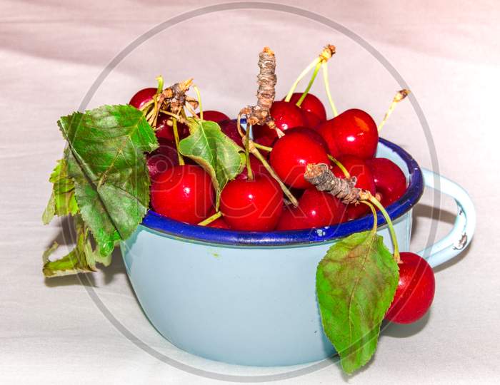 Fresh Cherries in the beautiful turquoise cup on wight background.