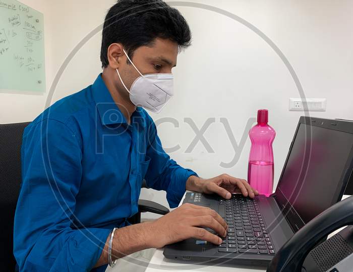 Man With Mask On Face Working On Laptop At Office.