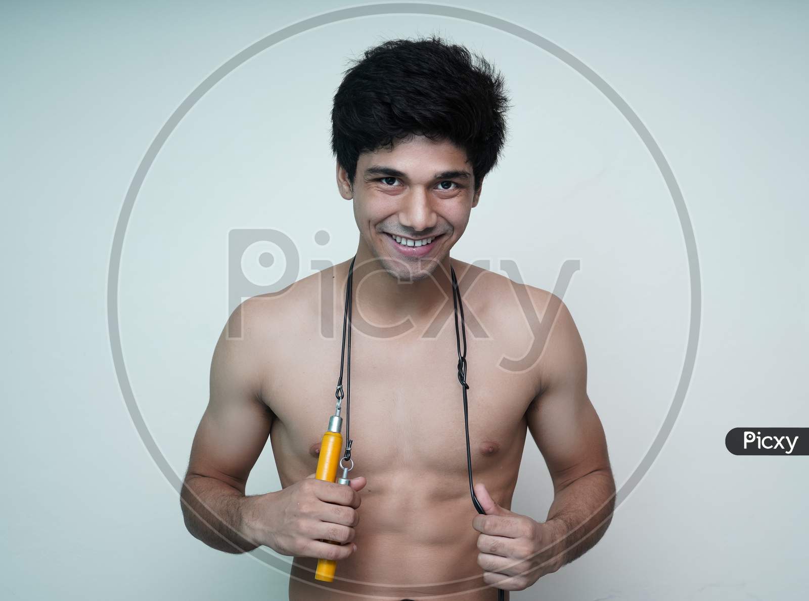 Image of Athletic Man With Naked Torso On A Bluish Background. Advertising  Fitness Trainer Smiling With Skipping Rope Around Her Neck.-JB660902-Picxy