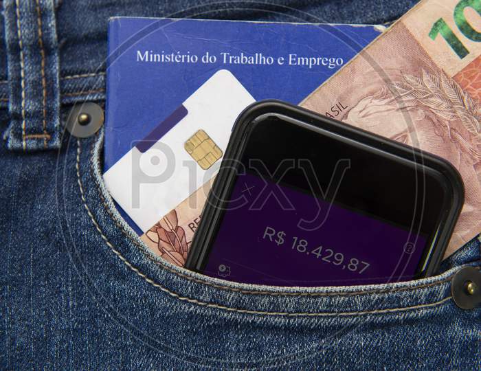 Close Up Of Cell Phone In Pocket Of Pants With Positive Bank Balance. Portfolio Of Work And Social Security. Real Banknotes. Formal Employment Concept. Translate: Ministry Of Labor And Employment.
