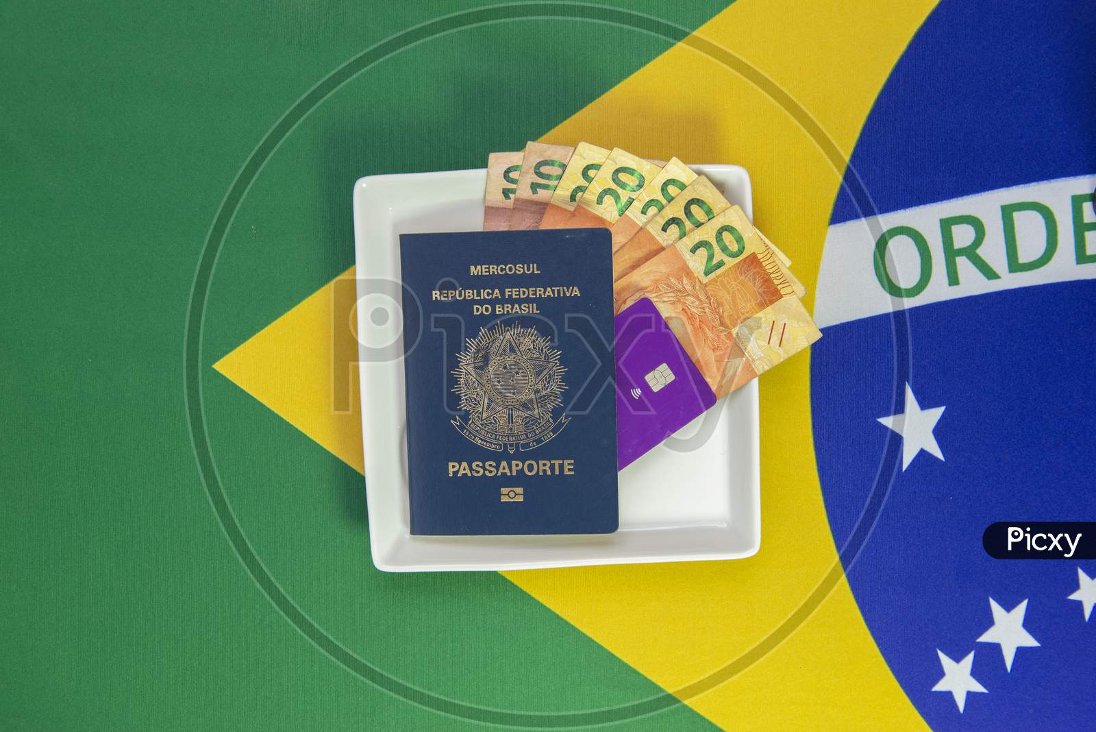 Brazilian Passport, Banknotes And Credit Card On A Square Plate With The Flag Of Brazil In The Background. Concept Of Travel And Shopping Expenses. Immigration And Emigration. Copy Space.