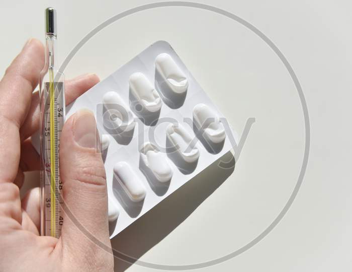 Thermometer, Humans Hand And Pack Of Pills On The White Background