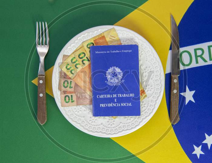Top View Of Brazilian Work Card On Plate Of Food With Cutlery Beside It. Brazilian Flag In The Background. Translate: Digital Work Card. Concept For Family Support.