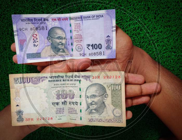 New And Old Indian Hundred Rupees Note Placed In Human Hand. Isolated On Green Background. Daylight