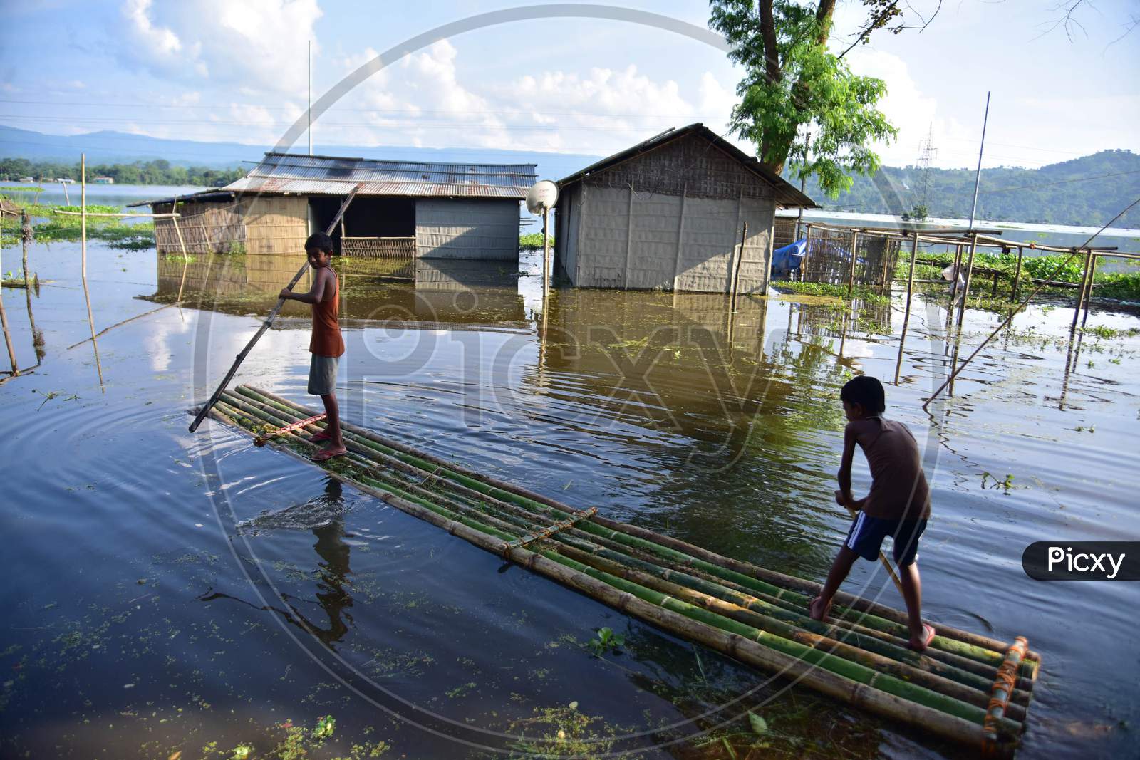 Boys Use  A Makeshift Raft To Cross Flood Waters Near Their Partially Submerged Hut At Baghmari Village Near Kaziranga In Nagaon District Of Assam On June 30,2020..