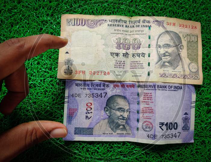 Hand Holding Of New And Old Indian Hundred Rupees Notes. Isolated On Green Background. Daylight.
