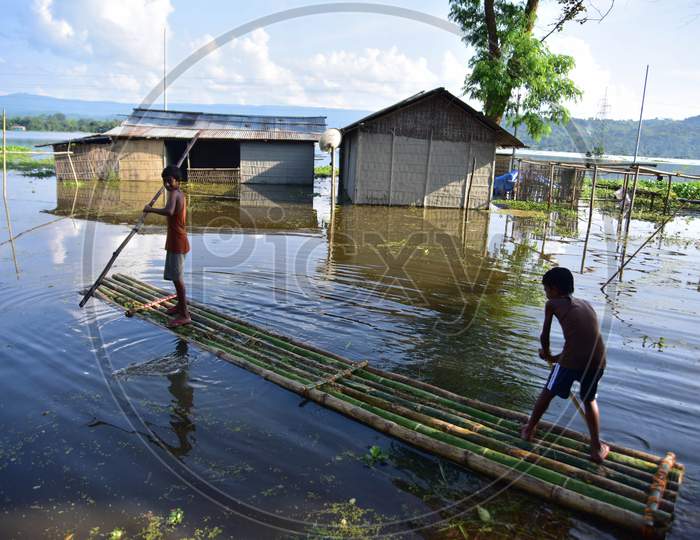 Boys Use  A Makeshift Raft To Cross Flood Waters Near Their Partially Submerged Hut At Baghmari Village Near Kaziranga In Nagaon District Of Assam On June 30,2020..