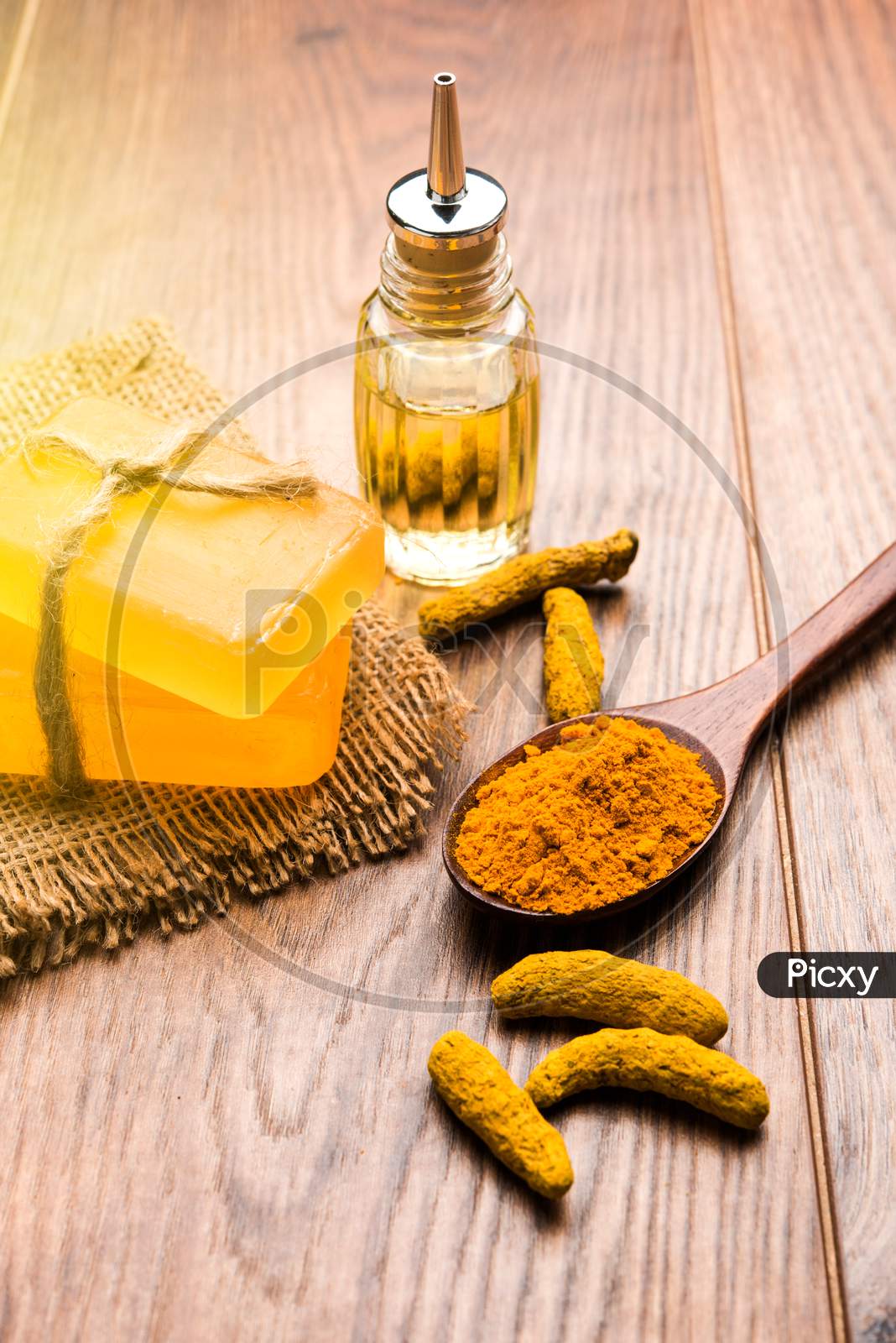 Turmeric essential oil with soap and raw Haldi sticks and powder in a wooden spoon