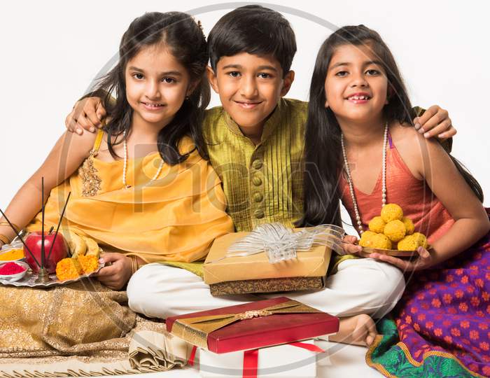 3 indian kids in traditional wear enjoying sweets and gifts on Rakhi or Bhai dooj