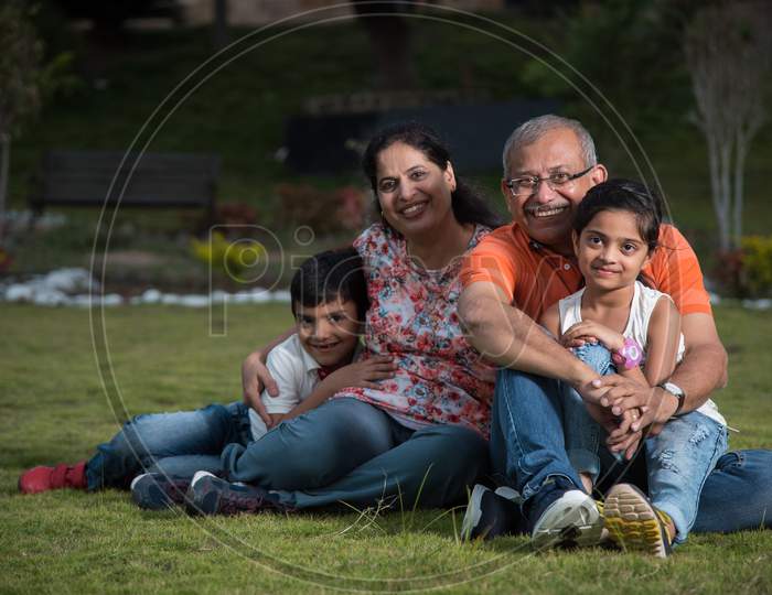 Portrait of Happy Indian/Asian Family - grand parents sitting on Lawn with kids / grandkids, outdoor