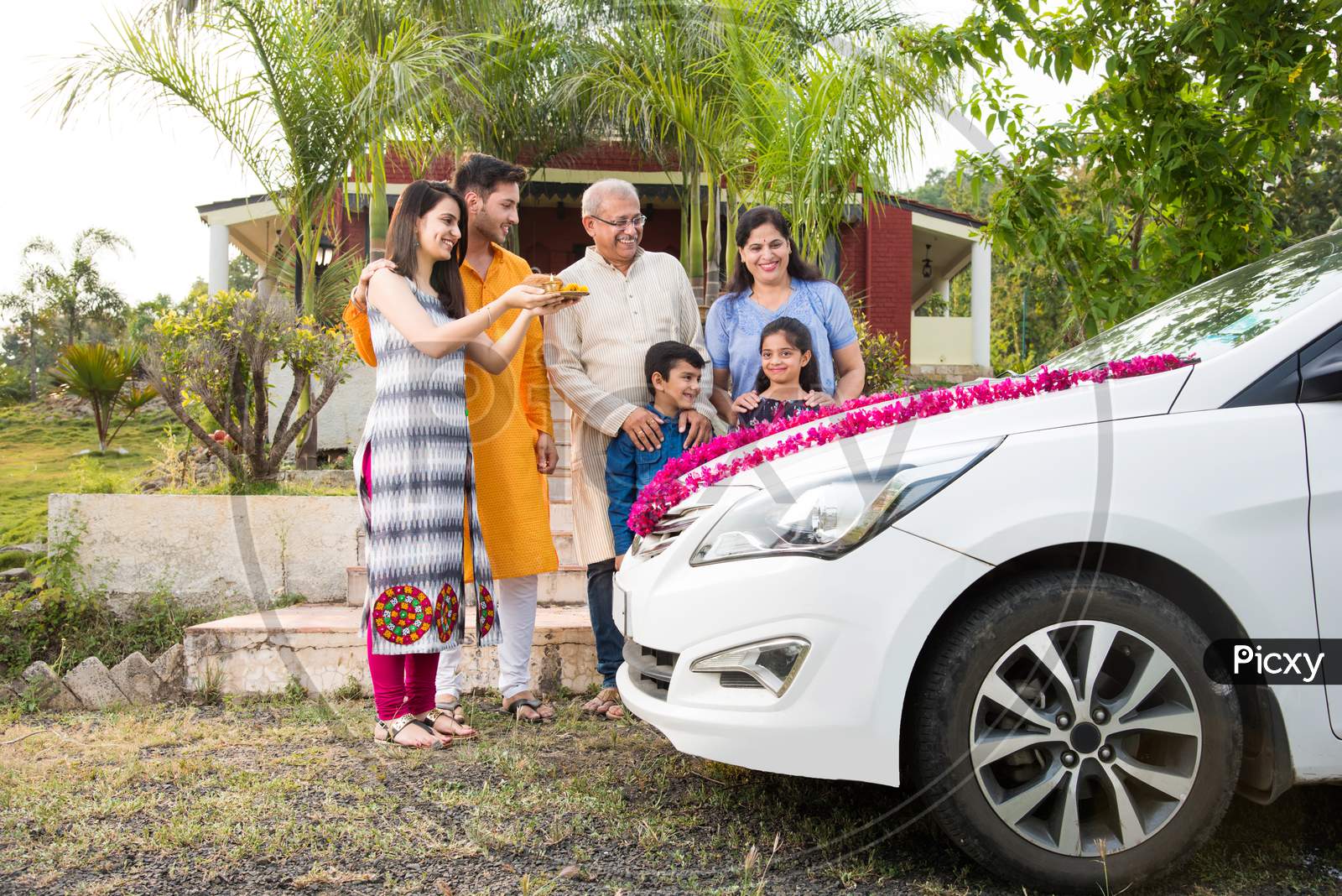 new car buying concept - indian family welcoming new car with puja thali and sweets