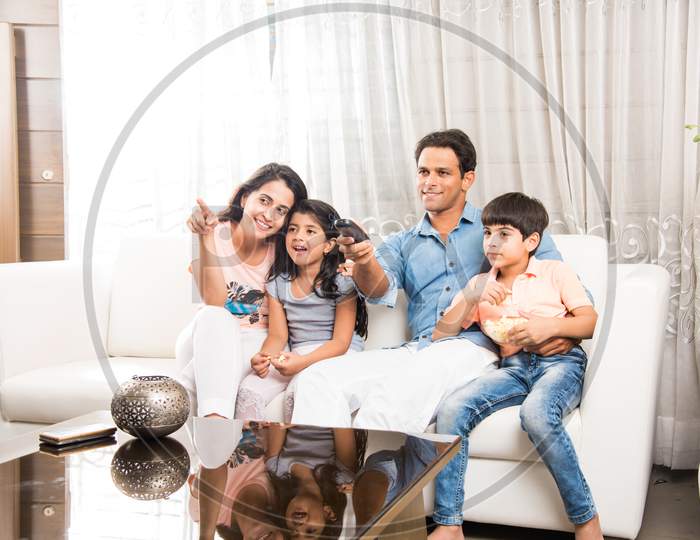 Indian family watching television / Tv while sitting on sofa