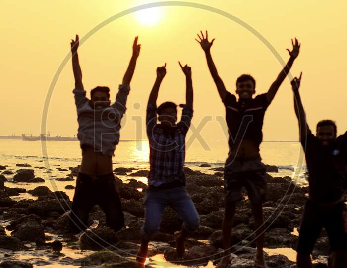 A Group By Four Young Man Jumping Activity During Sunset At Sea Beach .