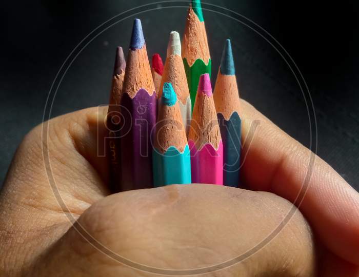 hand holding some colour pencils in black background with some selective focus