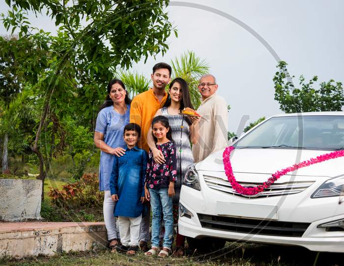new car buying concept - indian family welcoming new car with puja thali and sweets