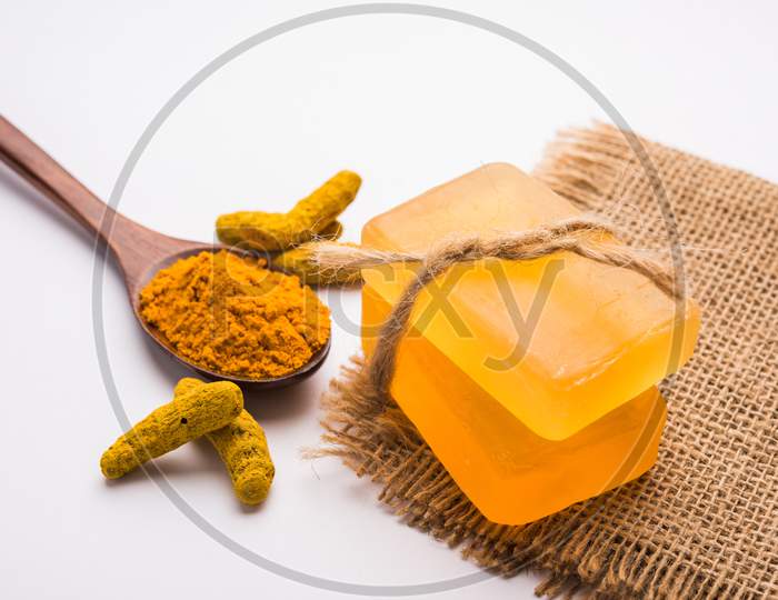 Turmeric essential oil with soap and raw Haldi sticks and powder in a wooden spoon