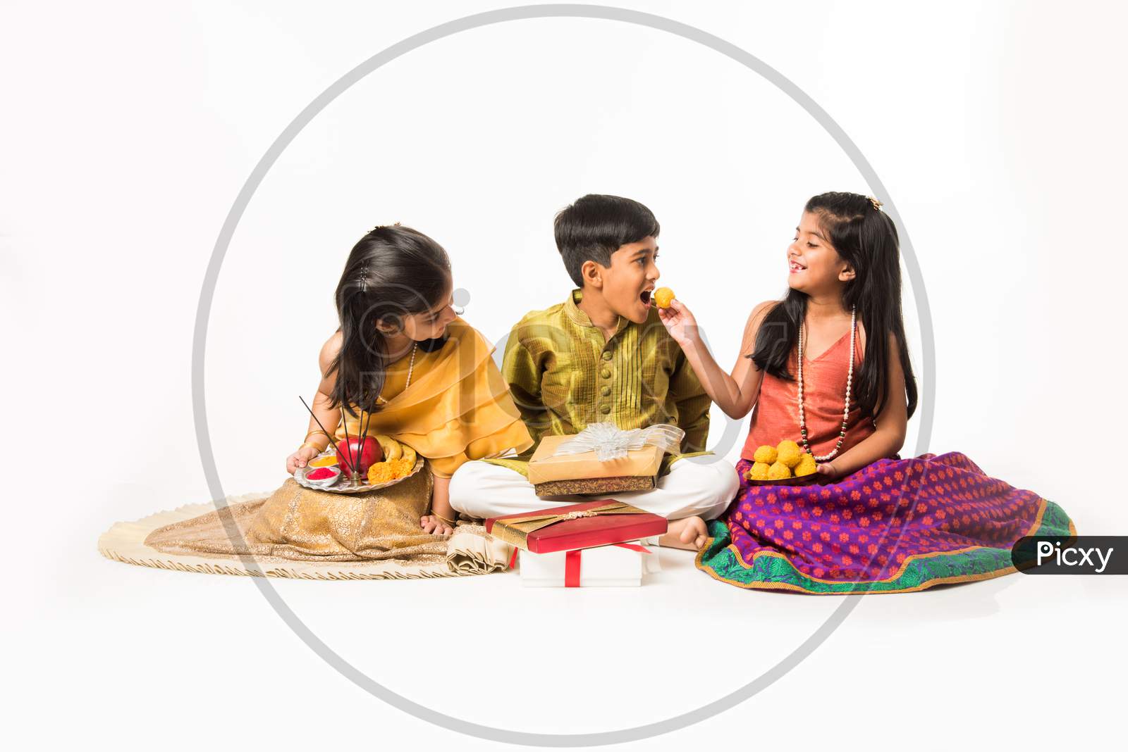 3 indian kids in traditional wear enjoying sweets and gifts on Rakhi or Bhai dooj