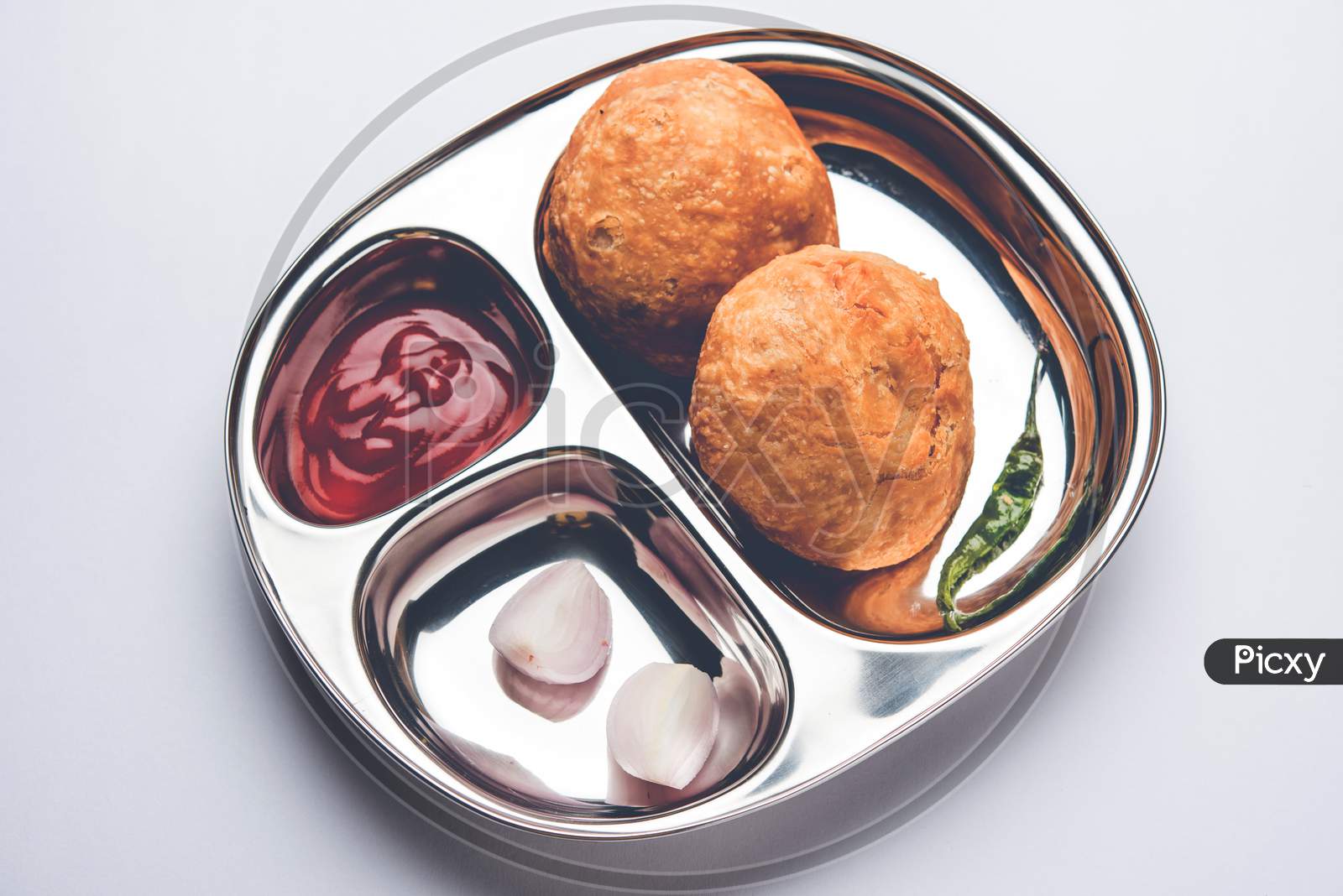 Kachori snack served in steel plate with tomato ketchup and onion