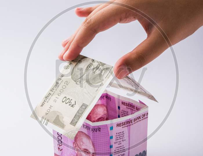 Hand holding 3D Model house using Indian currency