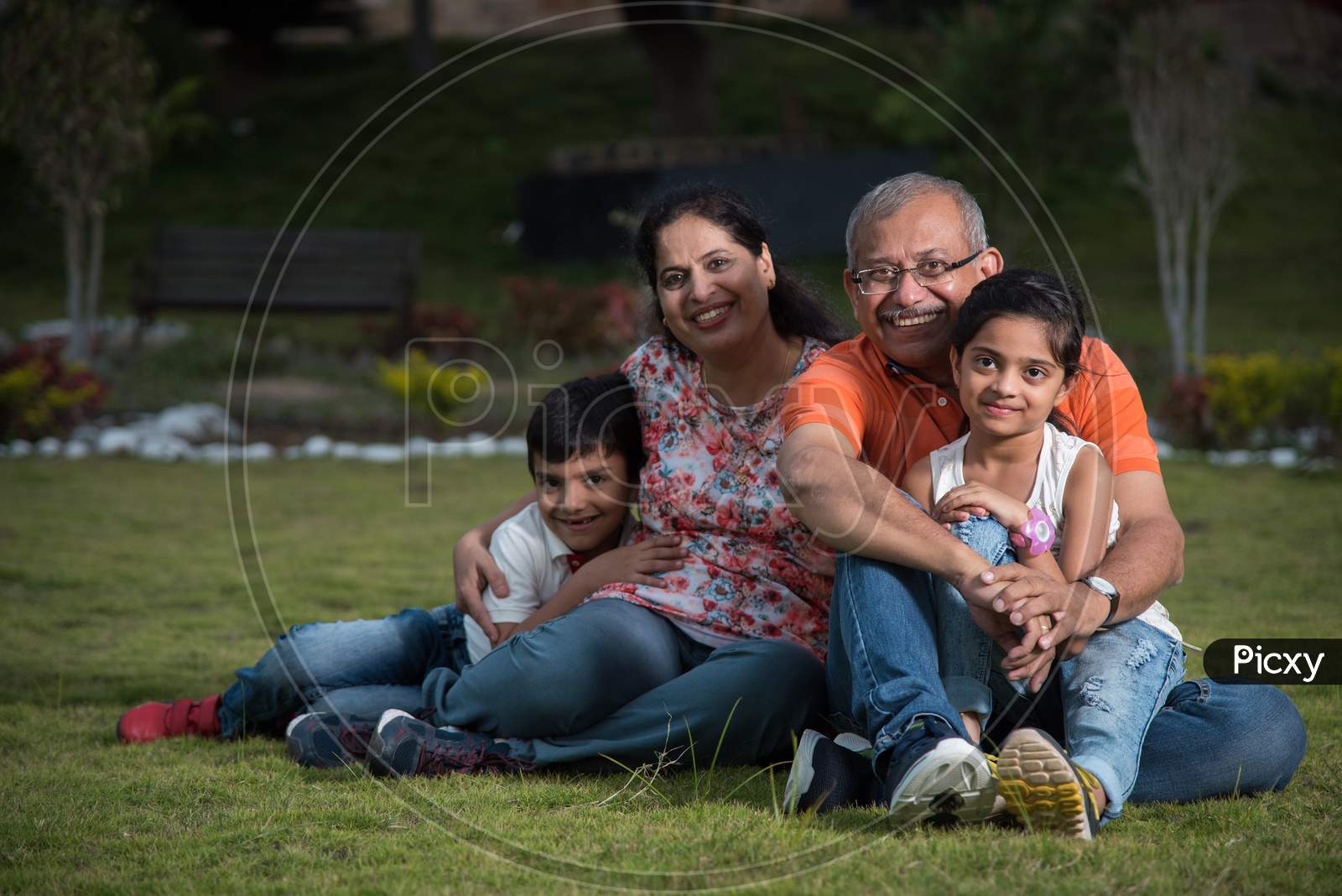 Portrait of Happy Indian/Asian Family - grand parents sitting on Lawn with kids / grandkids, outdoor