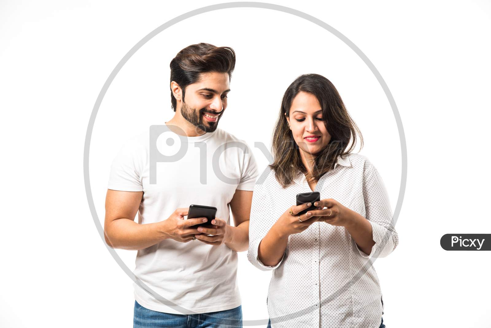 Indian couple using smartphone / mobile handset, standing isolated over white background