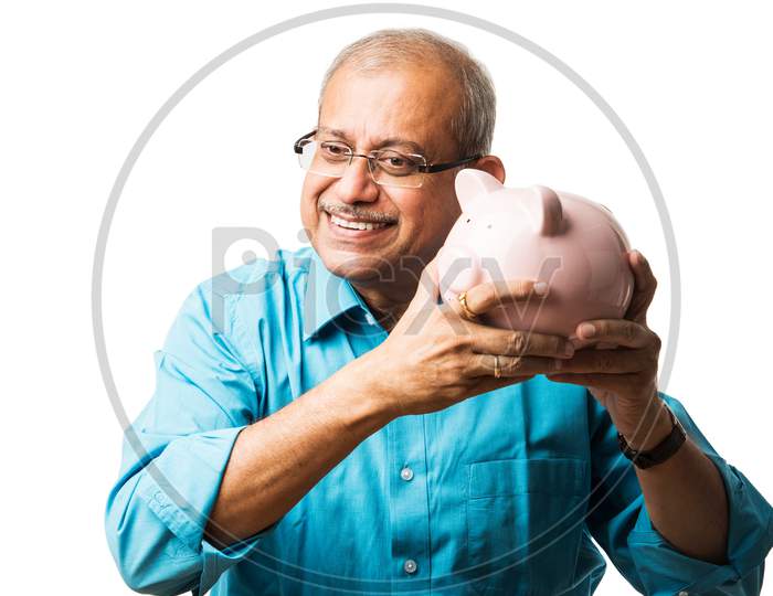 senior Indian/asian man and savings concept - with piggy bank, currency notes, 3d house model, money fan, pile of coins. sitting