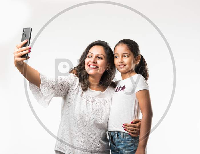 Indian/asian mother daughter taking selfie picture with smartphone, isolated over white background
