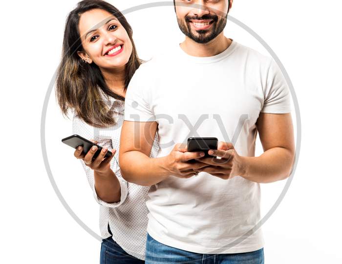 Indian couple using smartphone / mobile handset, standing isolated over white background