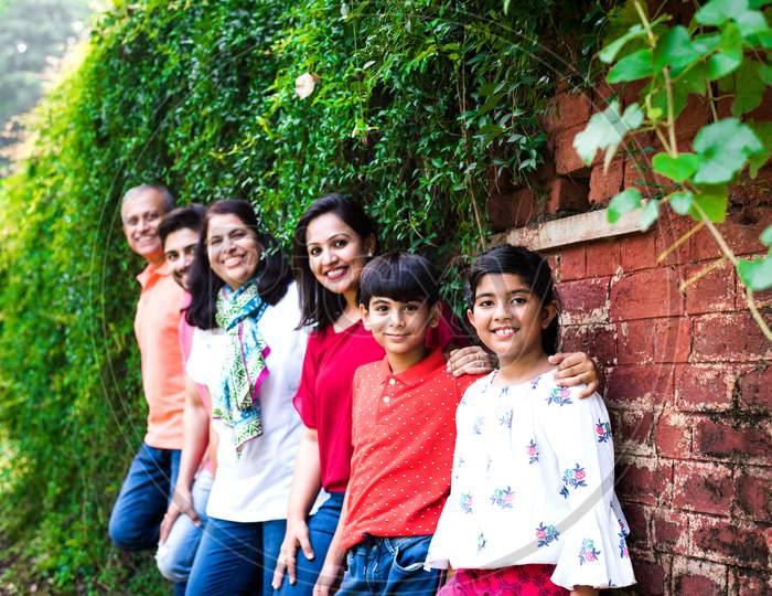 Multi generation Indian family of six standing against brick wall in park or garden and having fun, healthy family life concept