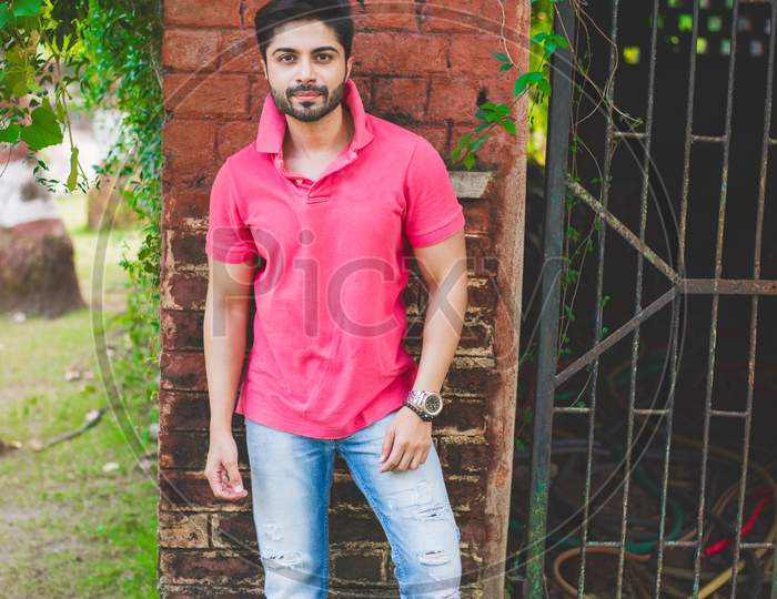Bearded Indian young man outdoor, standing against red brick wall at garden / park