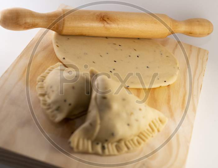 Uncooked Indian Samosa on a rolling board with uncooked Tortilla and rolling pin