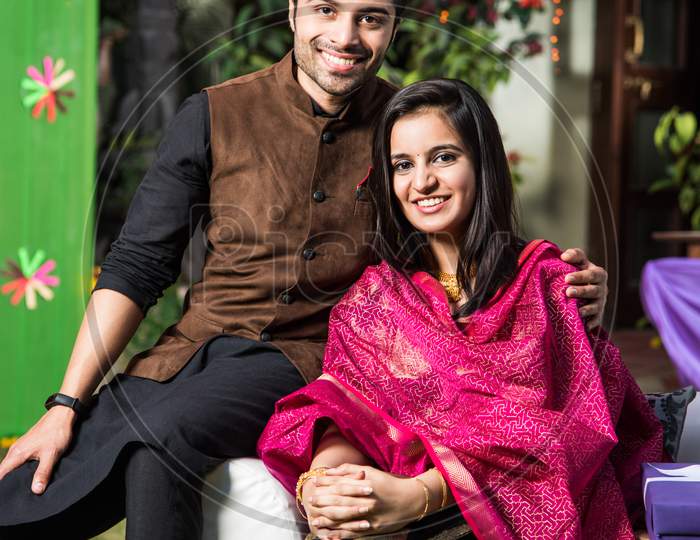 Indian young couple sitting on couch while celebrating diwali / festival or in wedding ceremony