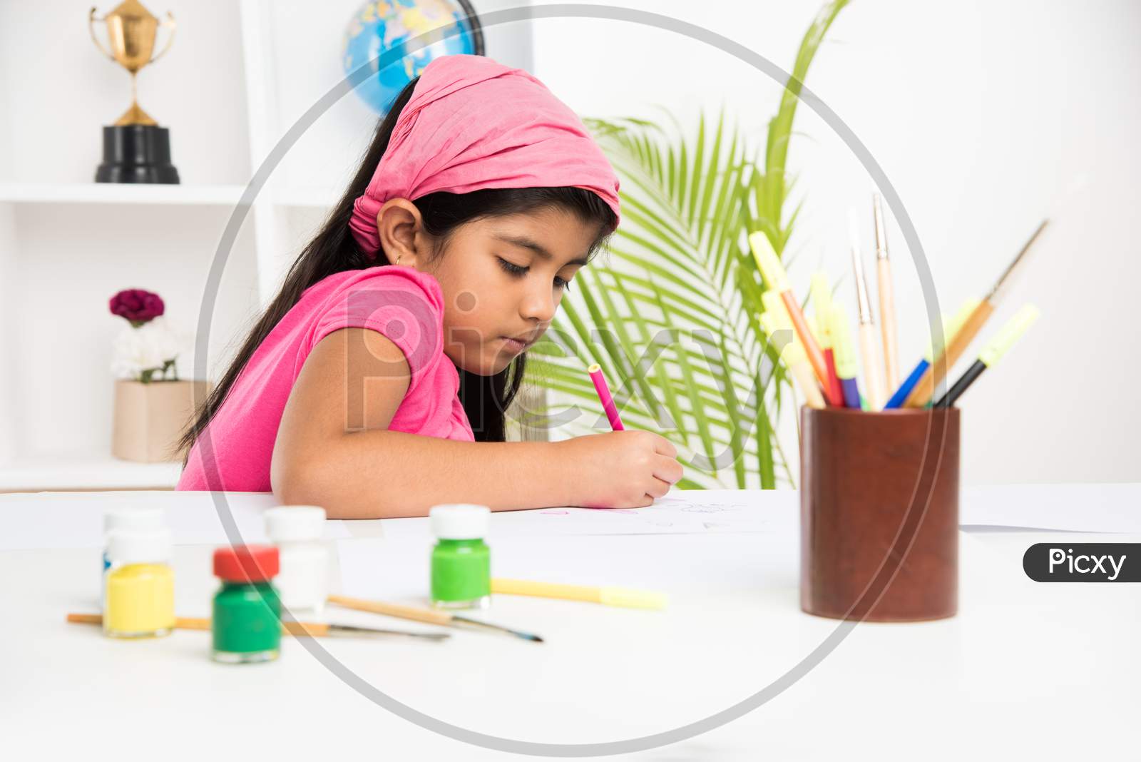 Cute Little Indian/Asian girl child enjoying drawing OR painting with brush and paint over paper at home
