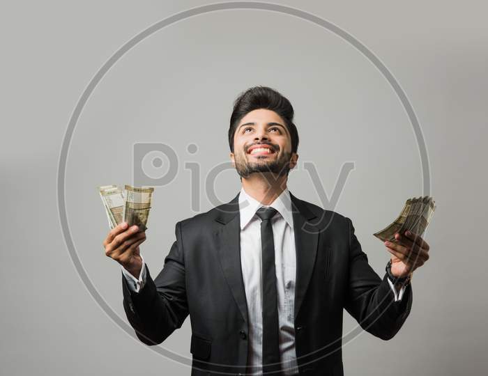 Happy bearded Indian businessman holding fan in hand, Indian Rupee currency bills of 500 , standing isolated over white backgrou